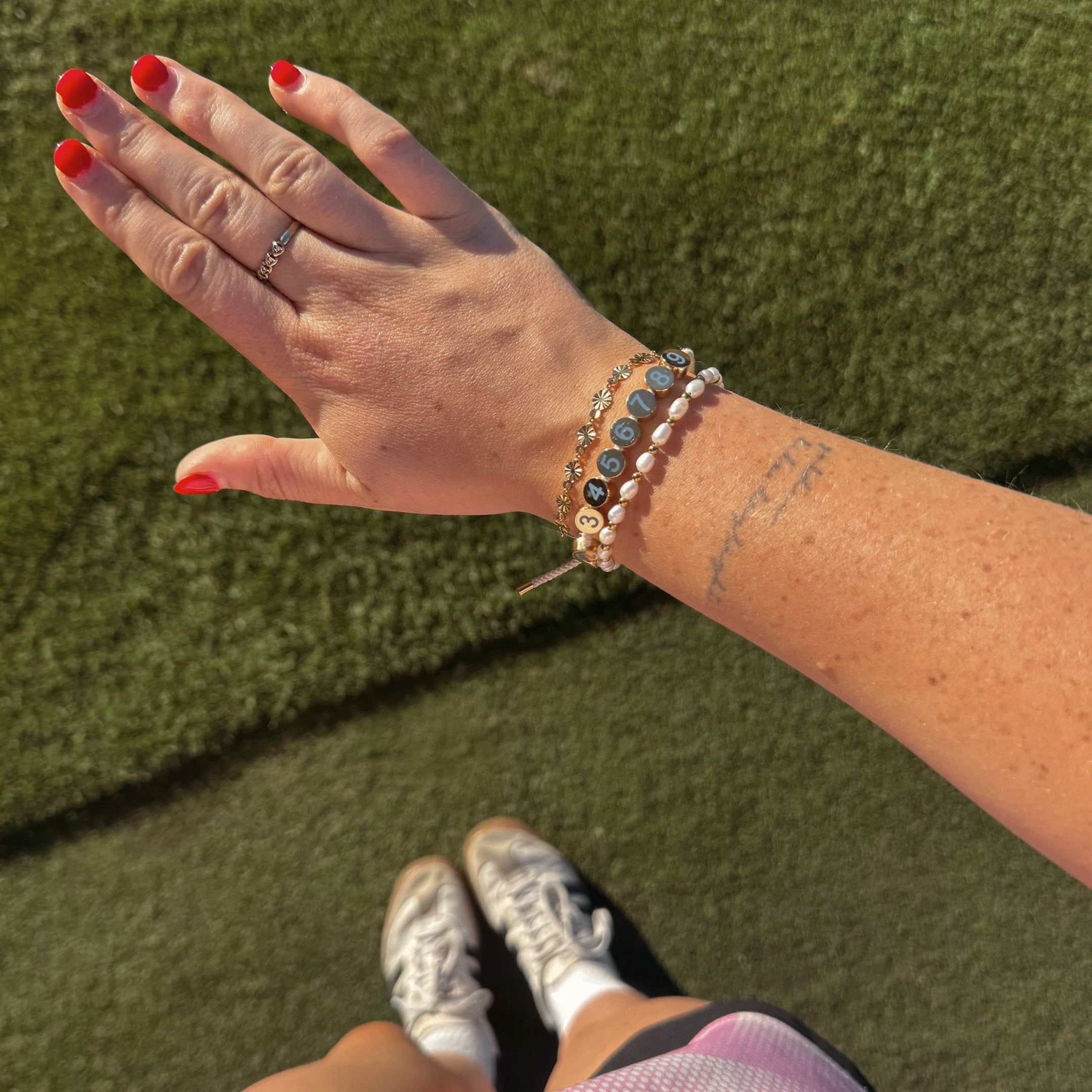 Hand with a score counter bracelets and red nail polish against a green grass background